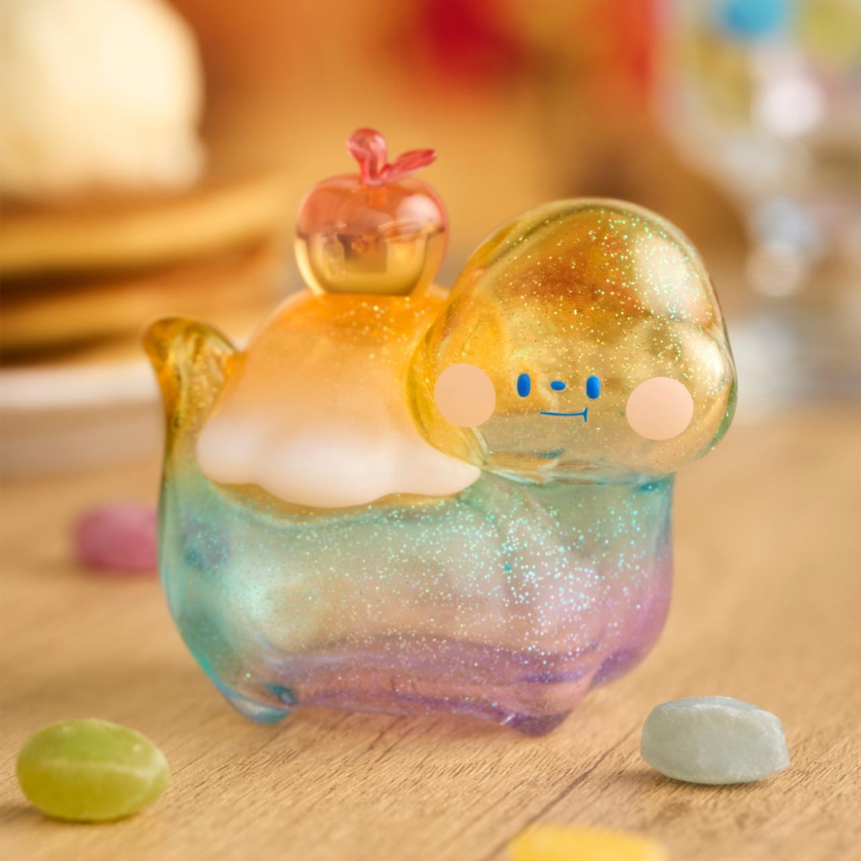 Colorful glittery figurine with a small pink character on top, sitting on a wooden surface.