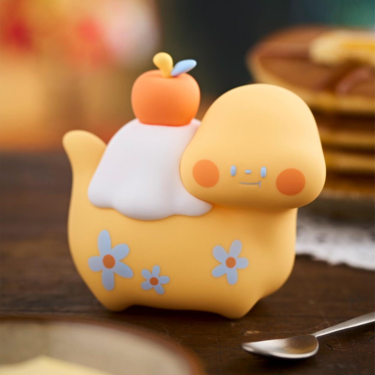 Yellow plush toy with a small orange fruit on top, sitting on a wooden surface.