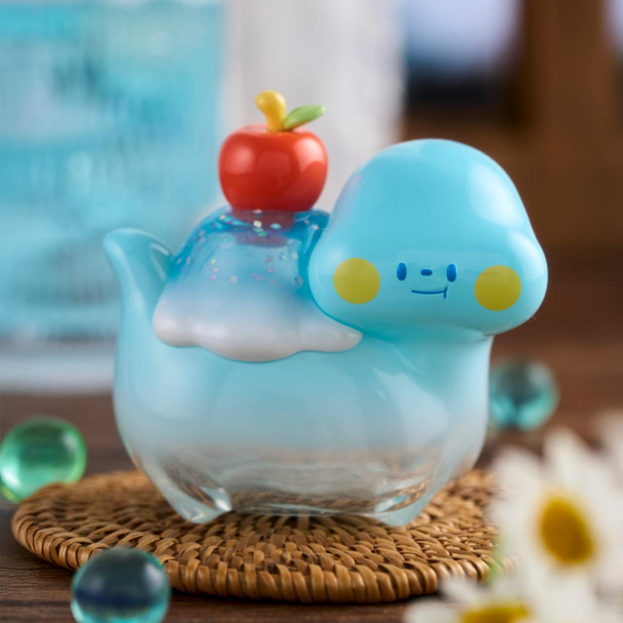 Cute glass figurine with a blue face and red apple on a woven coaster