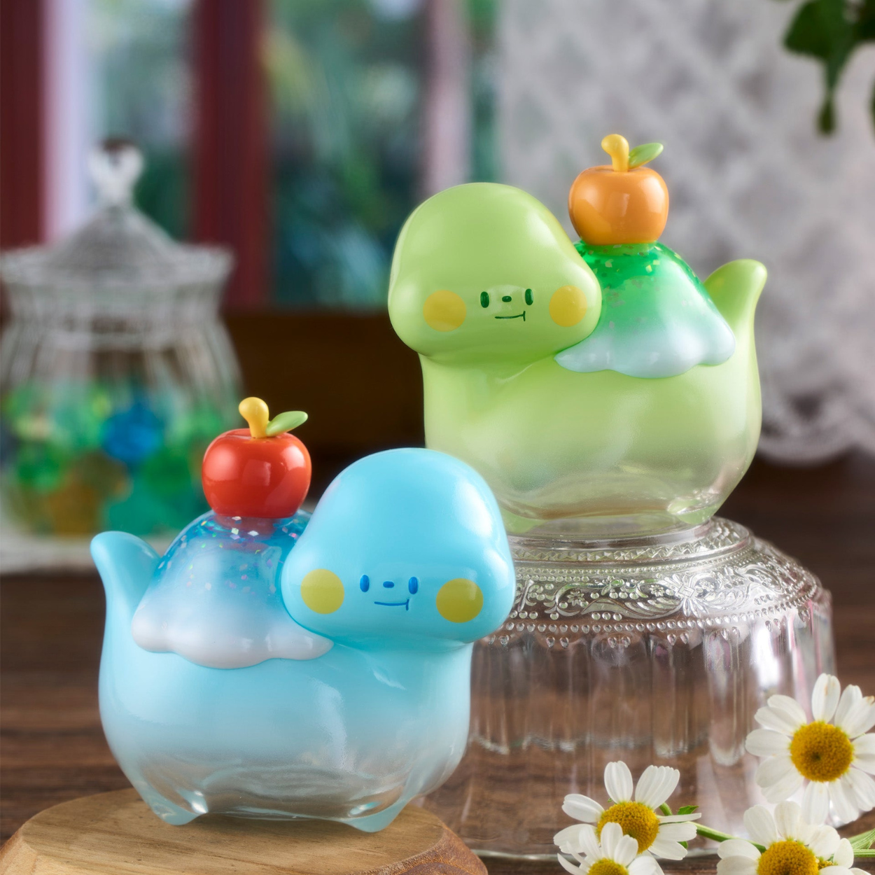 Two colorful glass figurines on a wooden surface with flowers in the background