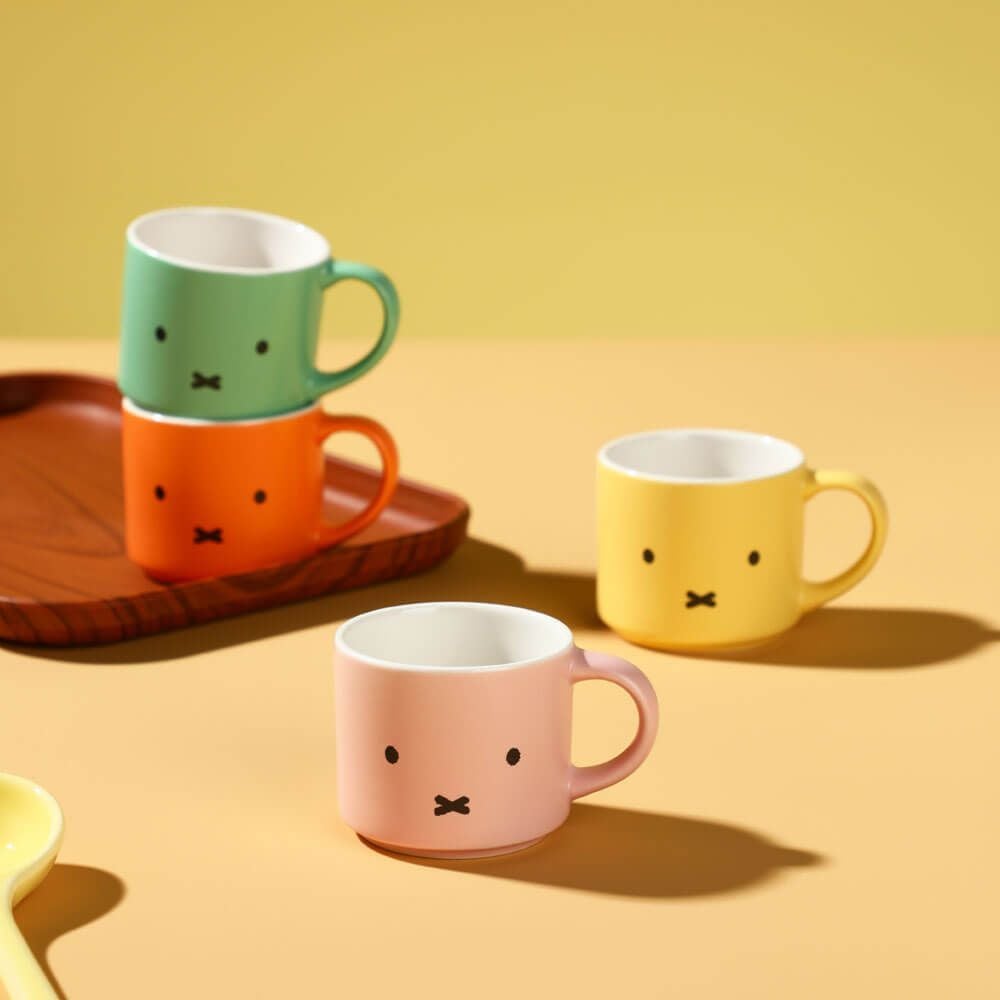 Four colorful mugs with facial expressions on a yellow background