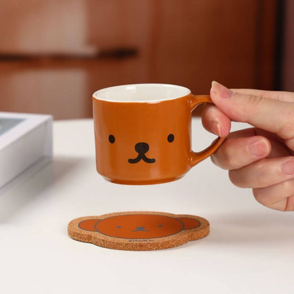 Person holding a brown mug with a bear face design on a white surface.