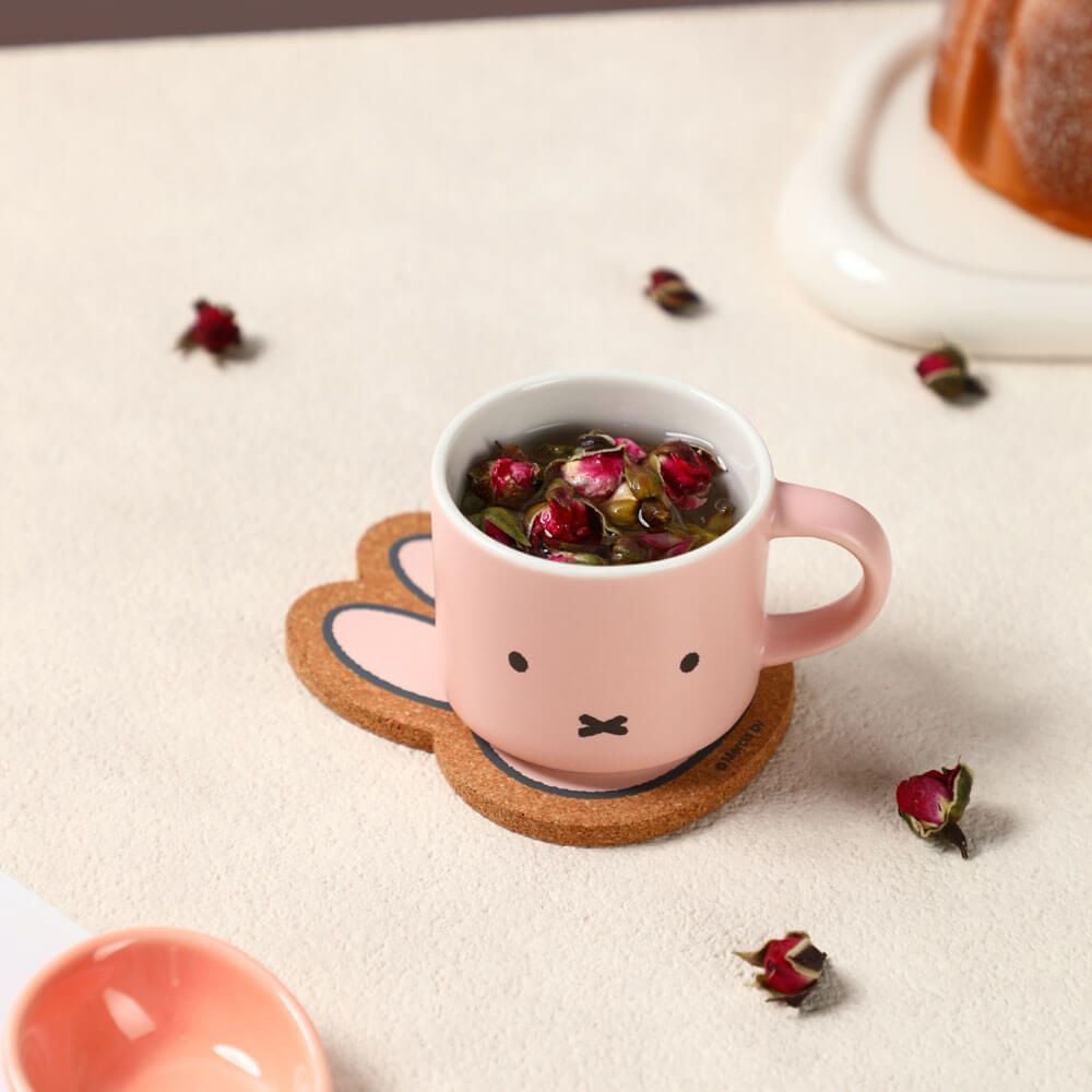 Pink mug with a face design filled with tea and dried flowers on a white surface.