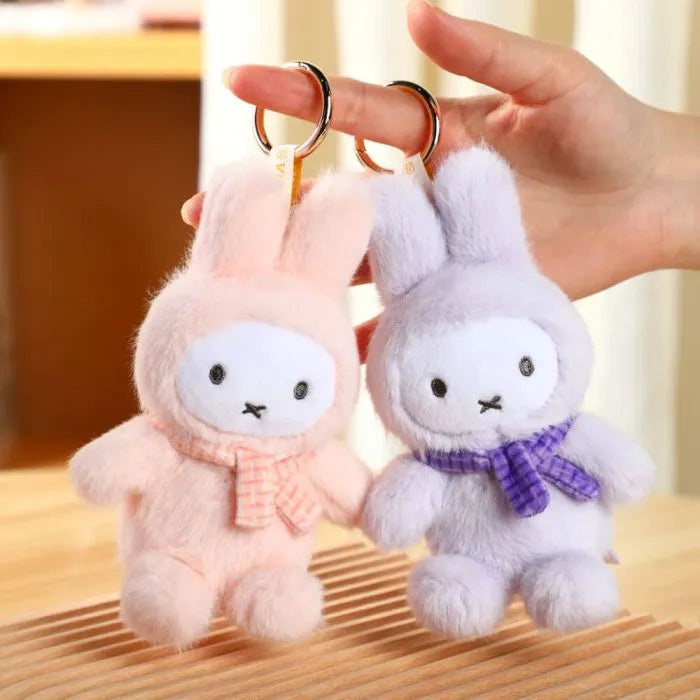 Two plush rabbit keychains, one pink and one gray, held by a hand on a wooden surface.