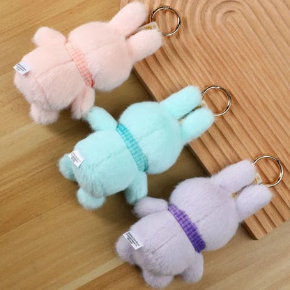 Three plush keychains shaped like dogs in pink, green, and purple on a wooden surface.