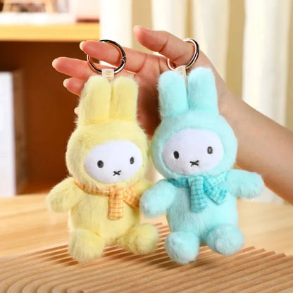 Two plush keychains, one yellow and one blue, held by a hand on a wooden surface.